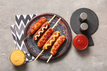 Plate with tasty corn dogs and bowls of different sauces on grey background