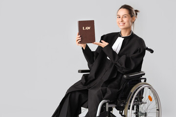Female judge in wheelchair with law book on light background