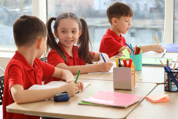 Cute little pupils writing at table in classroom. School holidays concept