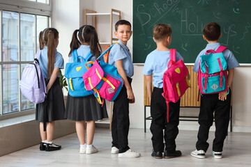 Cute little pupils with backpacks in classroom, back view. School holidays concept