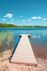 Tranquil wooden dock on a peaceful lake under a bright sunny sky, with fluffy clouds and lush green...