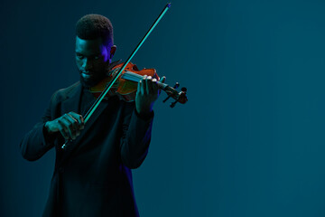 Musician in elegant black suit playing the violin on a vibrant blue background, creating a...