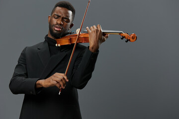 African American man in black suit playing violin on gray background, musician performing classical music concerto