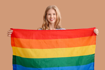 Beautiful young happy woman with LGBT flag on beige background