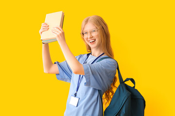 Female happy medical assistant with books on yellow background