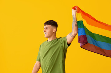 Handsome young happy man with LGBT flag on yellow background