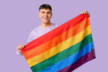 Handsome young happy man with LGBT flag on purple background