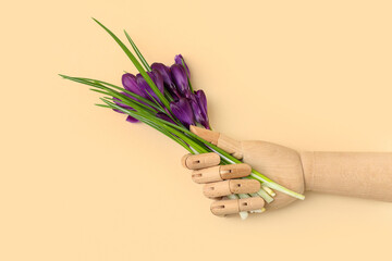 Wooden hand with beautiful crocus flowers on beige background