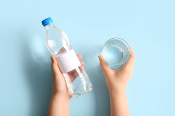 Female hands with plastic bottle of clean water and glass on blue background - obrazy, fototapety, plakaty