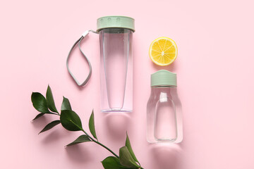 Sport bottles of clean water, lemon and leaves on pink background