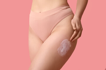 Beautiful young woman with anti-cellulite cream on pink background, closeup