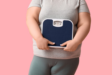 Young overweight woman with scales on pink background, closeup. Weight loss concept