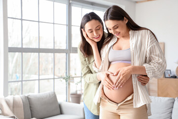 Young pregnant woman with her wife touching belly at home