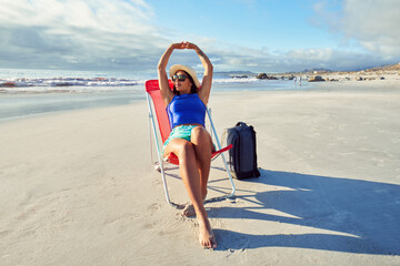 Latin american traveler woman sitting alone on a beach chair relaxing with arms raised on the shore...