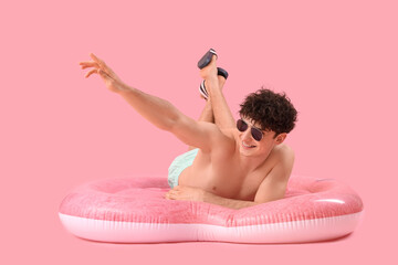 Handsome young happy man with inflatable mattress in shape of heart lying on pink background