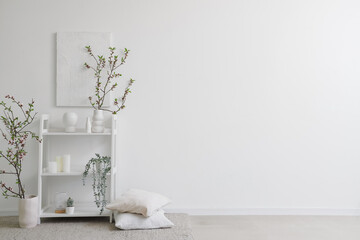Vases with blooming branches and decor on shelving unit near white wall