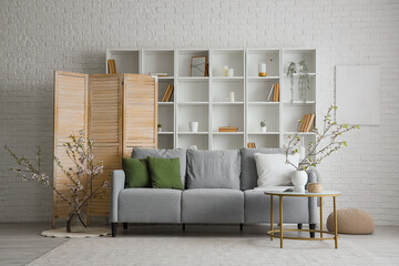 Grey sofa and vase with blooming branches on coffee table in interior of modern living room