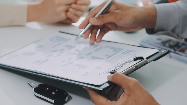 Man signing car insurance document or lease paper. Writing signature on contract or agreement. Buying or selling new or used vehicle. Car keys on table. Warranty or guarantee. Customer or salesman.