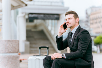 出張・旅行でバス停・タクシー乗り場・待合所でスマホで通話する外国人ビジネスマン
