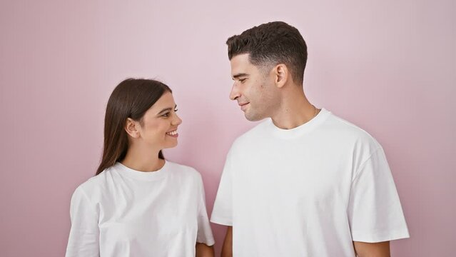 A man and woman in love, exchanging smiles in white t-shirts against a pink wall, embodying beauty and romantic relationship.
