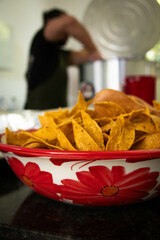 String tortilla chips on white and red bowl and chef cooking in background