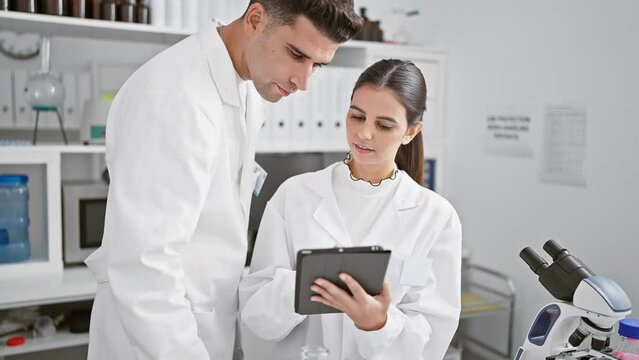 A man and woman, depicted as scientists, collaborate using a tablet in a modern laboratory environment.