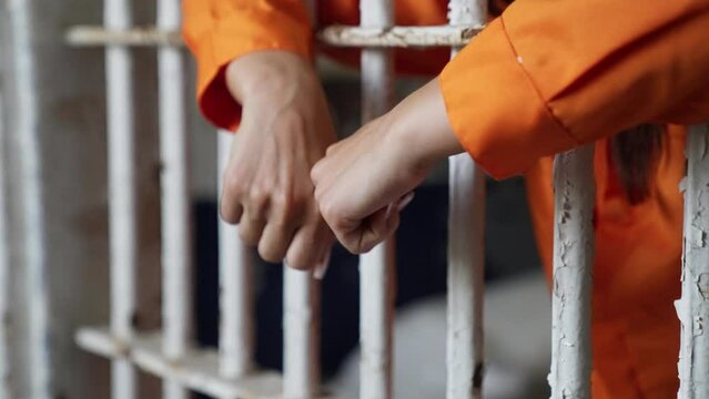 Female Woman Prisoner in Orange Jumpsuit Prison in Jail Cell Hands on Bars
