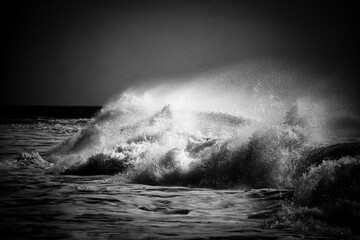 Raging waves crash against the shore, tumultuous and wild, under stormy skies.