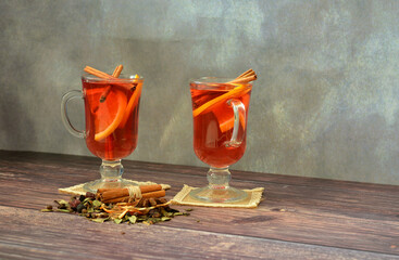 Two glasses of hot wine with spices and citruses on a wooden table.