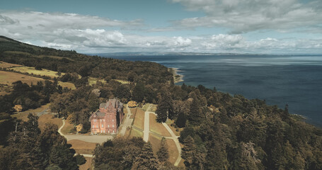 Scotland's landscape, medieval castle aerial view: trees and ocean shore at Brodick Bay, Arran Island. Majestic scenery of green leafy wood at coastline. Beauty of Scottish nature. Cinematic shot