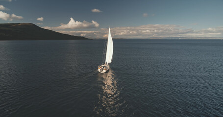 Alone sail yacht reflect at ocean water surface aerial. Racing sailboat at open sea. Luxury vessel at summer cruise scenery. Cinematic soft sun light over wide serene seascape. Scenic marine shot