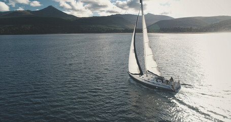 Sun over luxury yacht at ocean coast aerial. Majestic sailboat regatta race at sea bay. Sunlight...