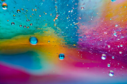 Closeup through window of colorful water spreading over glass surface against multicolored blurred background