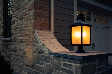 Fototapeta na wymiar Illuminated Post Lantern Casting a Warm Glow on A Stone House Wall