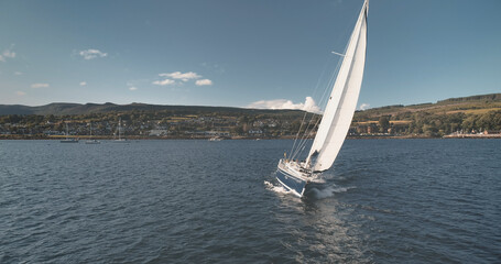 Yacht sailing at ocean bay aerial. Summer nobody nature seascape. Sailboat at sun reflection. Port town cityscape at sunny mountain shore. Amazing landscape. Epic cruise at open sea. Marine vacation