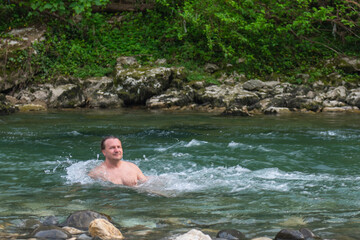 Adventurous Man Enjoying a Refreshing Swim in a Serene Mountain River Surrounded by Trees and Rocks