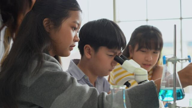 group of asian school kid pupil student looking through microscope together during science practical class in school laboratory. asia children scientists learning biology chemistry lesson .