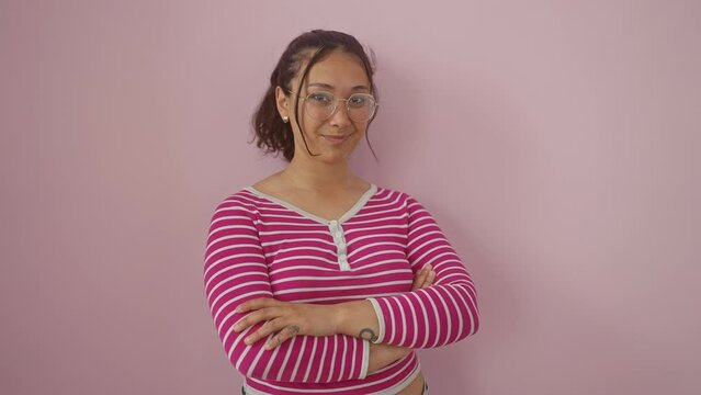 Young hispanic woman wearing stripes t shirt standing happy face smiling with crossed arms looking at the camera. positive person. over isolated pink background