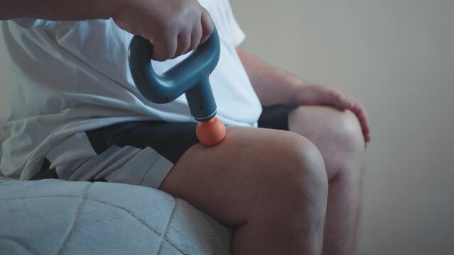 Massage percussion gun at work. Elderly man massaging leg muscles, caring for failure in the elderly with new technology.