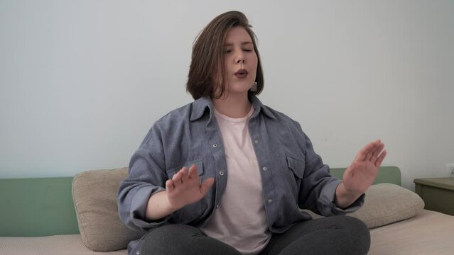 Woman practicing breathing techniques, seated in lotus pose on sofa at home.