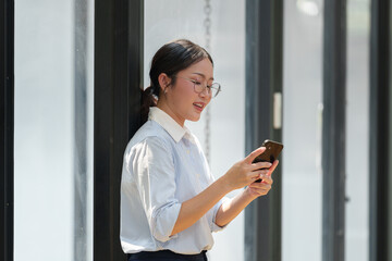 Happy Asian businesswoman in glasses standing smiling looking at data Talk on the phone using your...