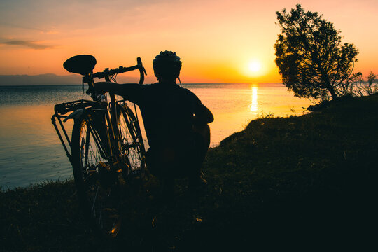 Silhouette cyclist traveler by his bicycle enjoy sunset view together by tranquil Sevan lake nature. Bicycle touring outdoors in nature. Self care and recreational sports activities. Weekend get away 