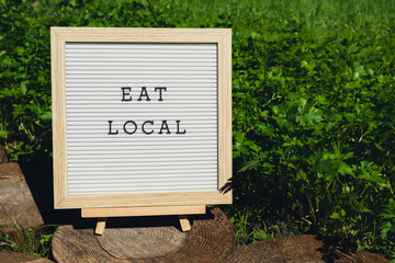 Letter board with text EAT LOCAL on background of garden bed with green herb parsley. Organic farming, produce local vegetables concept. Supporting local farmers
