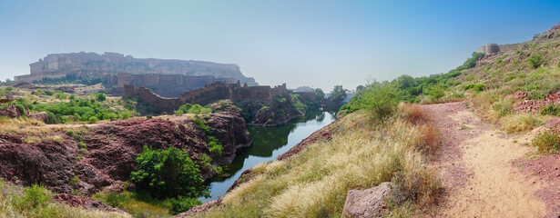 Panoramic view of Mehrangarh fort from Rao Jodha desert rock park, Jodhpur, India. A lake in foreground and Mehrangarh fort in the background, with rocky landscape of the desert park.