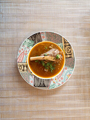 Round patterned plate with indian food dish made with lamb meat called Nihari on textured background