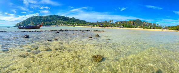 Panoramic view of Phi Phi Islands Beach with Crystal Ocean Waters and Blue Skies. Long-tail Boat (Reua Hang Yao) Anchored in the Background. Krabi Province, Thailand, Southeast Asia.