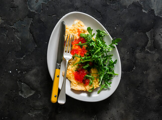 Cheese omelet with red caviar and arugula on a dark background, top view - 782779665