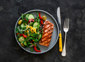 Delicious diet lunch, dinner - grilled salmon and fresh vegetable salad on a dark background, top view