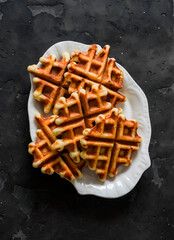 Orange peel and dried apricots waffles on a dark background, top view