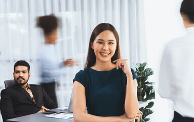 Young Asian businesswoman portrait poses confidently with diverse coworkers in busy meeting room in...
